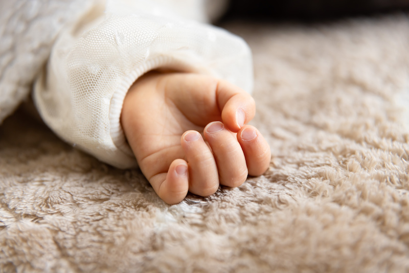 A left hand of sleeping asian baby on the carpet. High quality photo. 02.25.2023. This is an one years old kid's hand.